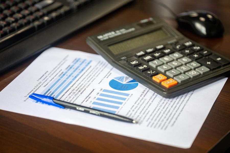 A desk calculator resting on a printed financial report with bar and pie charts