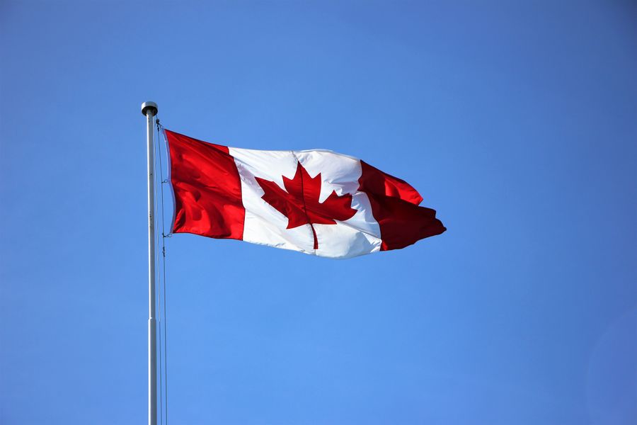 The Canadian maple-leaf flag flying from a pole against a clear blue sky