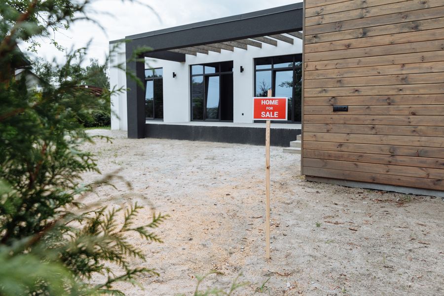 A red “Home for Sale” sign staked in the front yard of a modern house