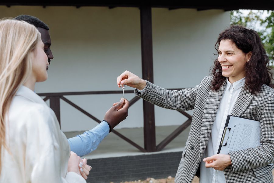 A real estate agent handing house keys to a smiling couple outside their new home