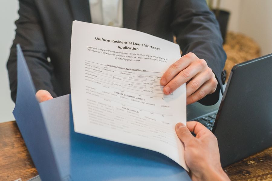 Hands holding a residential mortgage loan application form across a desk